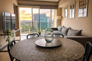 A modern living room with a round table, a sofa, and a large window offering a city view. - Modern Apartment in ParkLife |City View (Guadalajara)