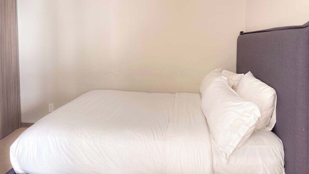 A single bed with white bedding in a room with plain walls and a visible electrical outlet. - Modern Apartment in ParkLife |City View (Guadalajara)
