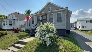 Ein einstöckiges Haus mit Veranda, ein kleiner Garten mit weißen Blumen und eine Flagge.