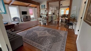 A spacious living area with a large rug, a grey sofa, and a dining table with chairs. - Riverview Cottage, a quaint downtown home with River and Park views (Millinocket)