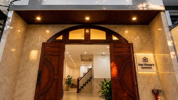 A hotel entrance with a marble facade, a wooden double door, a staircase, and a sign indicating 'Han House's Apartment.' - Han House's Apartment 1 (Da Nang)