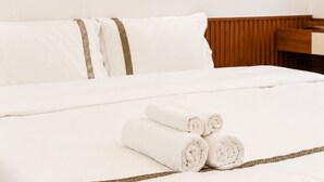 A neatly made bed with white linens and rolled towels, a wooden headboard, and a wooden desk. - Han House's Apartment 1 (Da Nang)