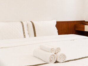 A neatly made bed with white linens and rolled towels, a wooden headboard, and a wooden desk. - Han House's Apartment 1 (Da Nang)