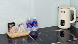 A kitchen counter with a kettle, two water bottles, a glass carafe, and a tray with a coffee pod and a box. - Han House's Apartment 1 (Da Nang)