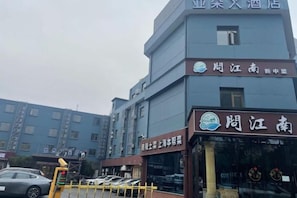 Un hôtel à plusieurs étages, avec un restaurant bien visible au rez-de-chaussée et un parking où sont stationnées des voitures.