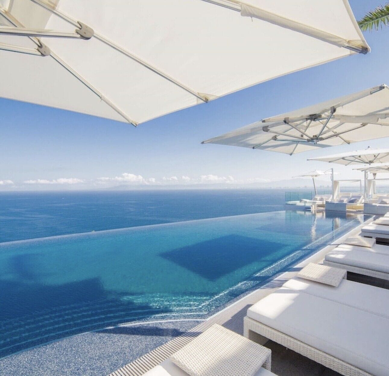 Ein Pool ohne Ende mit Liegestühlen und Sonnenschirmen, mit Blick auf ein klares, blaues Meer.