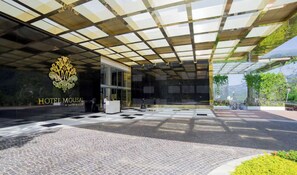 Entrada de hotel con marquesina de vidrio, mostrador de recepción y un logotipo.