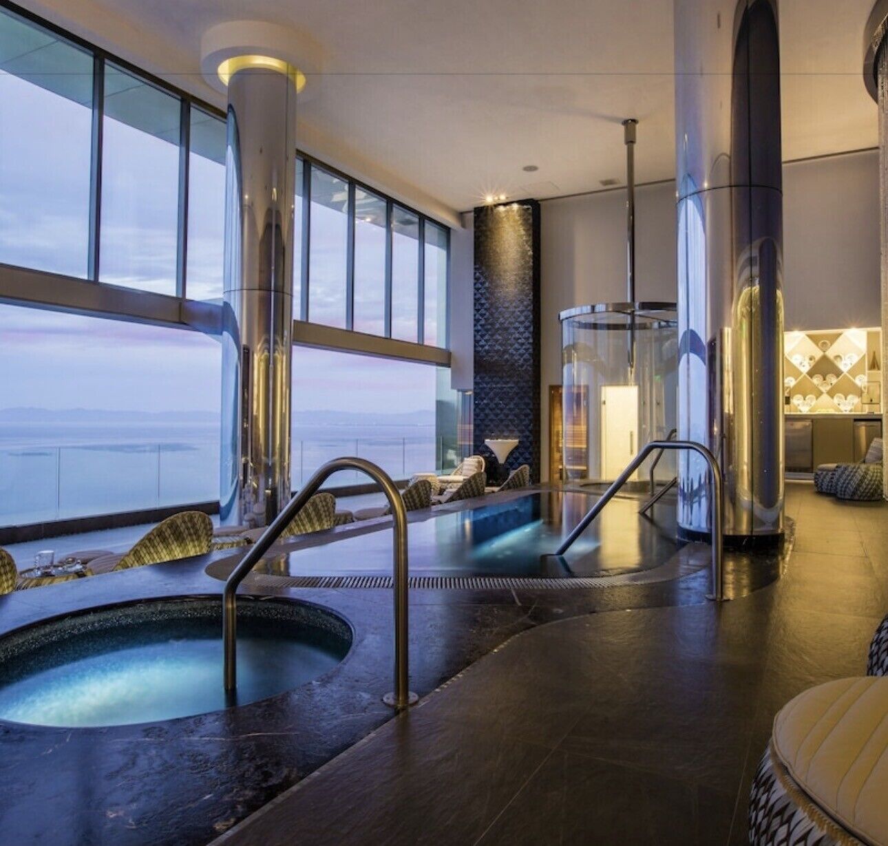 Ein Wellnessbereich mit zwei Whirlpools, einer Glasbrüstung und Blick aufs Meer.