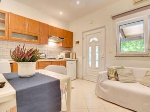 A compact kitchen with wooden cabinets, a microwave, and a dining area with a table and chairs. - Villa Delia by Interhome (Medulin)