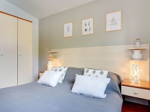 Un dormitorio con cama, mesitas de noche, armario y estanterías en la pared.