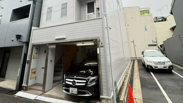 Un edificio a più piani con un accesso al garage, un'auto parcheggiata e una linea elettrica visibile.