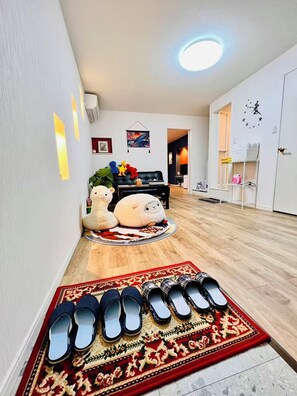 A living room with a sofa, a rug, slippers, and a wall clock.