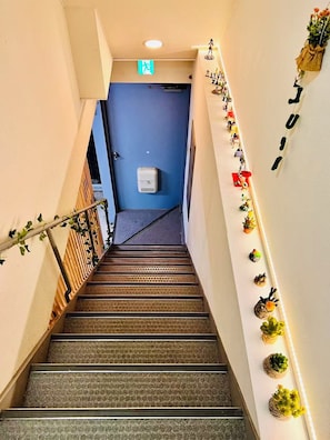 A staircase with a handrail, a blue door at the top, and small potted plants on the wall. - Direct KIX Train & 1 min Walk to Station - Vibrant Osaka 2BR Apt w/ AC (大阪市)