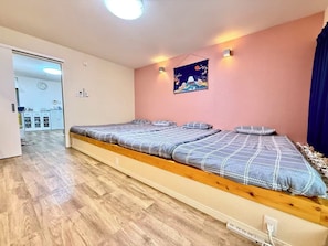 A room with a long bed, a kitchen area, and a wall clock. - Direct KIX Train & 1 min Walk to Station - Vibrant Osaka 2BR Apt w/ AC (大阪市)