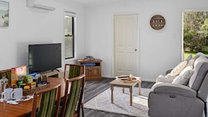 A living room with a TV, sofa, dining table, and a door. - Native Retreat - Tranquil Seaham Escape (Port Stephens)