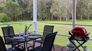 An outdoor patio with a table set for dining, surrounded by chairs, and a barbecue grill. - Native Retreat - Tranquil Seaham Escape (Port Stephens)
