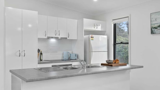 A modern kitchen with white cabinetry, a stainless steel sink, and a window with a view of greenery. - Native Retreat - Tranquil Seaham Escape (Port Stephens)