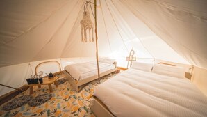 Ein Zelt mit zwei Betten, einer hängenden Makramee-Lampe und einem kleinen Tisch mit Tassen und einem Teekessel.