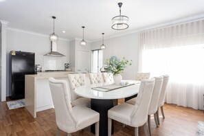A modern kitchen with a dining area, featuring a central island, pendant lights, and a large window with curtains. - Spacious 4BR Family Home • Pool with Spa & BBQ (Byford)