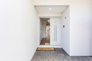 A hallway leading to a room with a door, a doormat, and a light fixture. - Spacious 4BR Family Home • Pool with Spa & BBQ (Byford)
