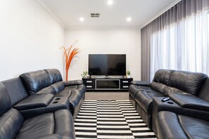 A modern living room with two black leather sofas, a flat-screen TV, and a black and white striped rug. - Spacious 4BR Family Home • Pool with Spa & BBQ (Byford)