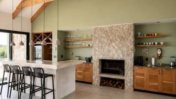 A spacious kitchen with a central island, wooden beams, and a stone fireplace.