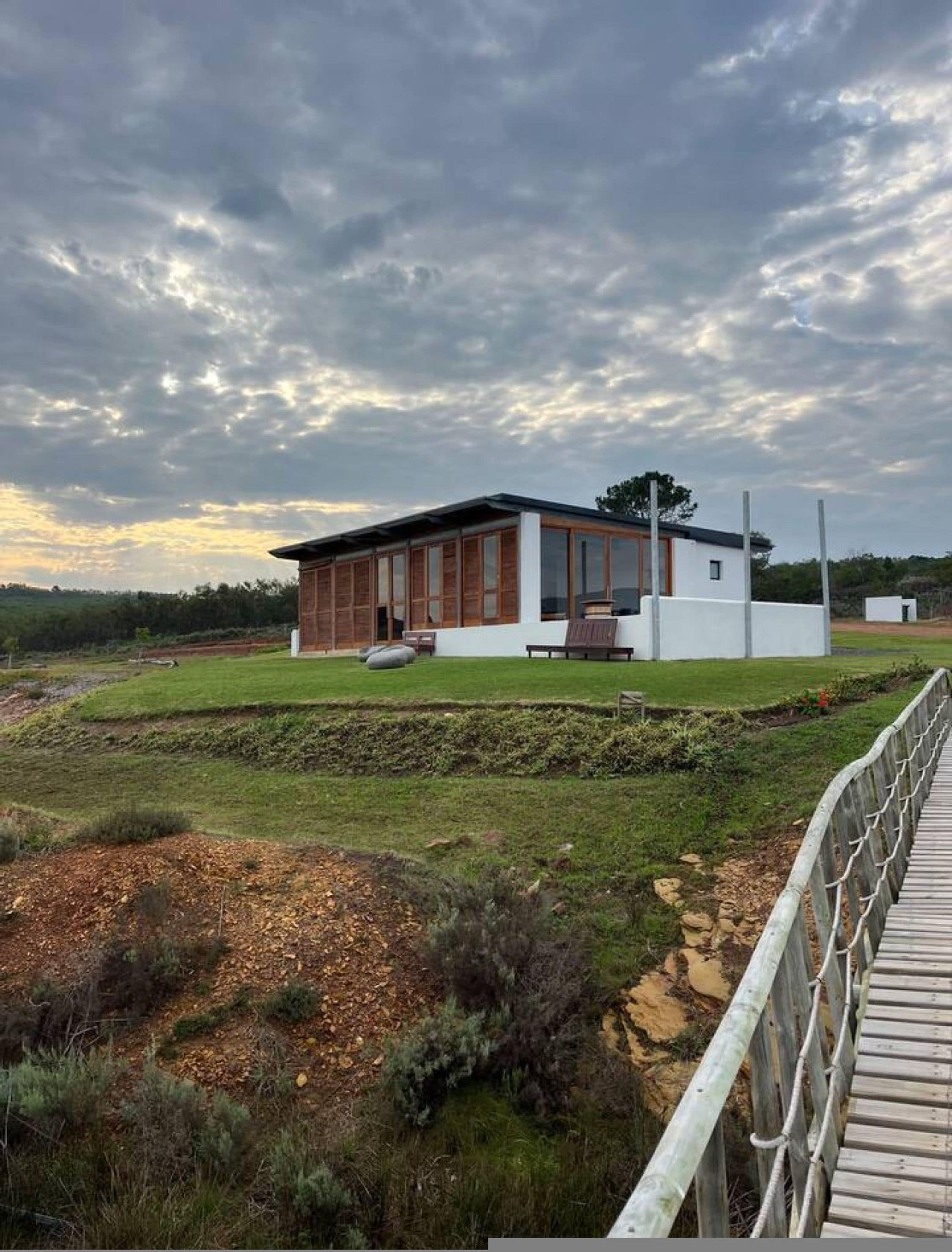 Una casa moderna con un amplio ventanal, una terraza de madera y un jardín cubierto de césped.