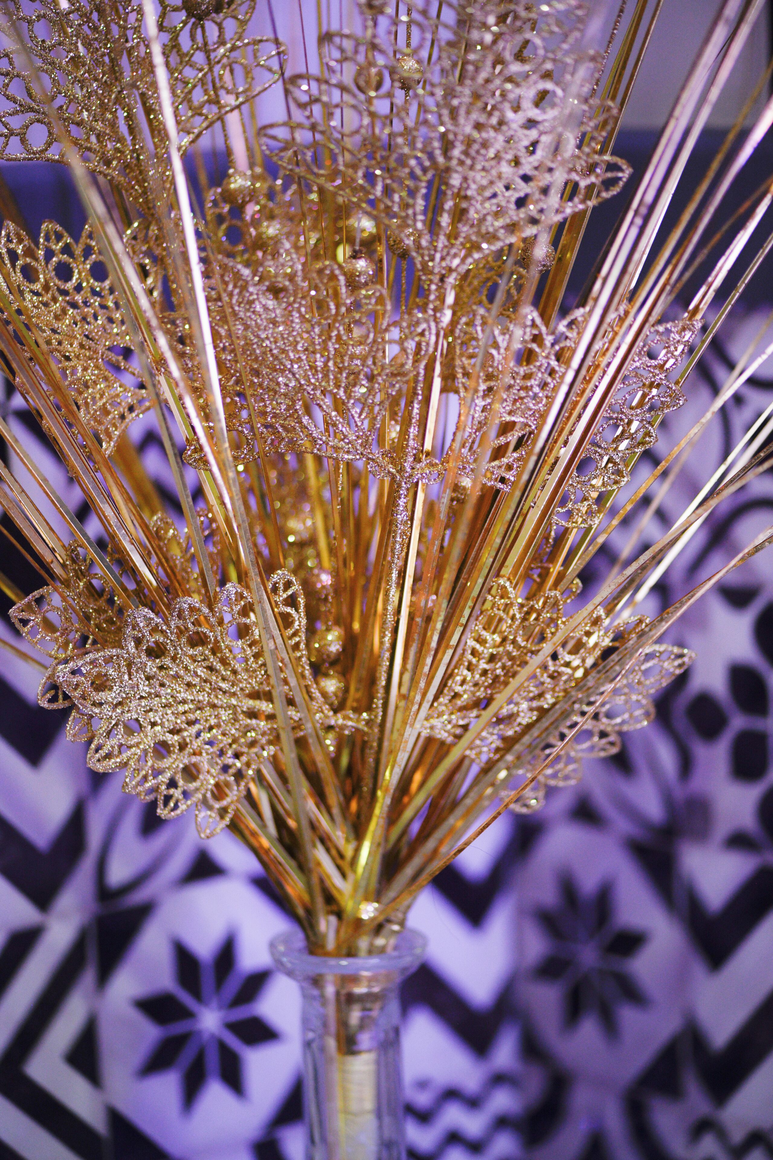 Un vase en verre transparent contenant un bouquet d’éléments décoratifs dorés.