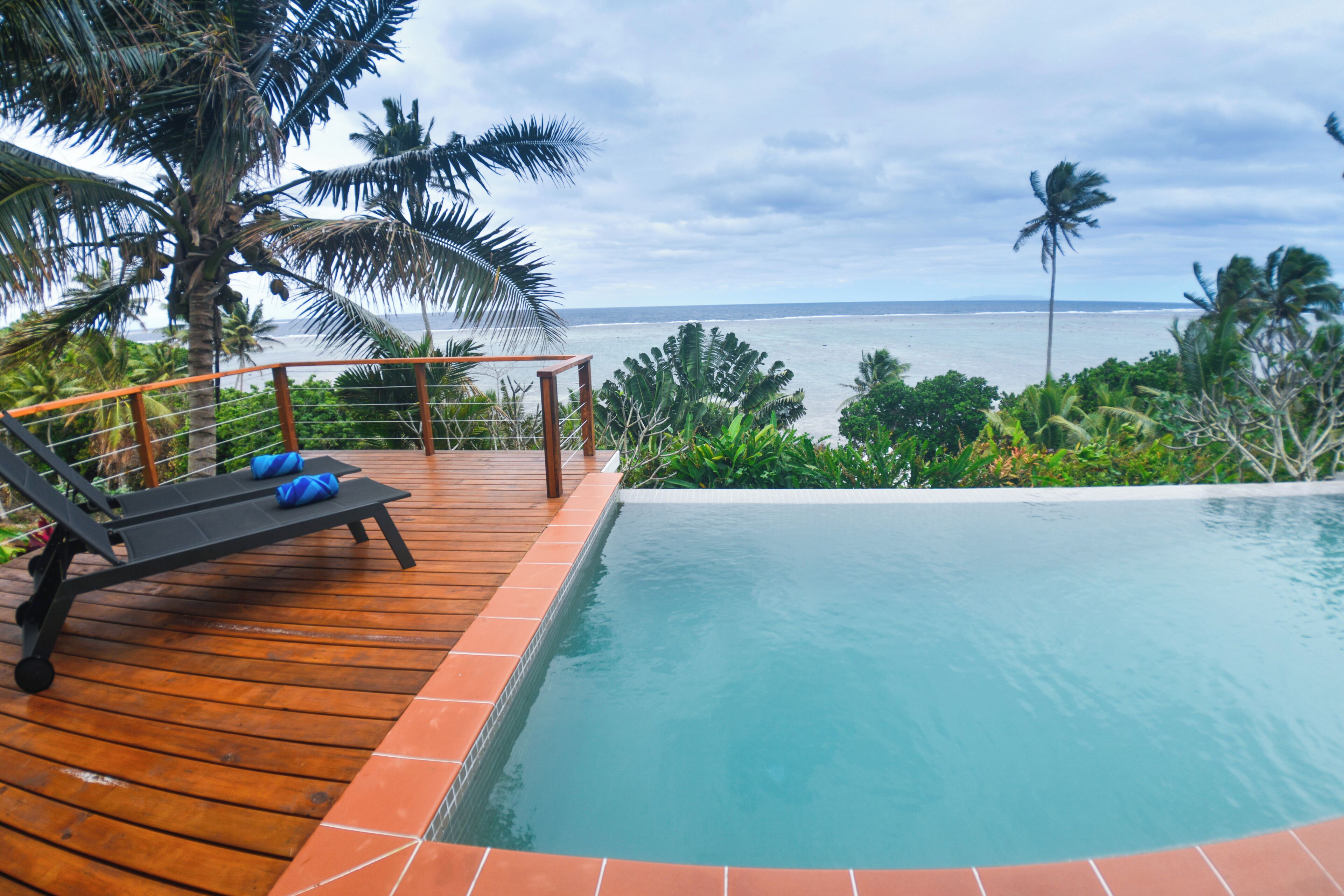 A wooden deck with a pool, lounge chairs, and a view of the ocean.