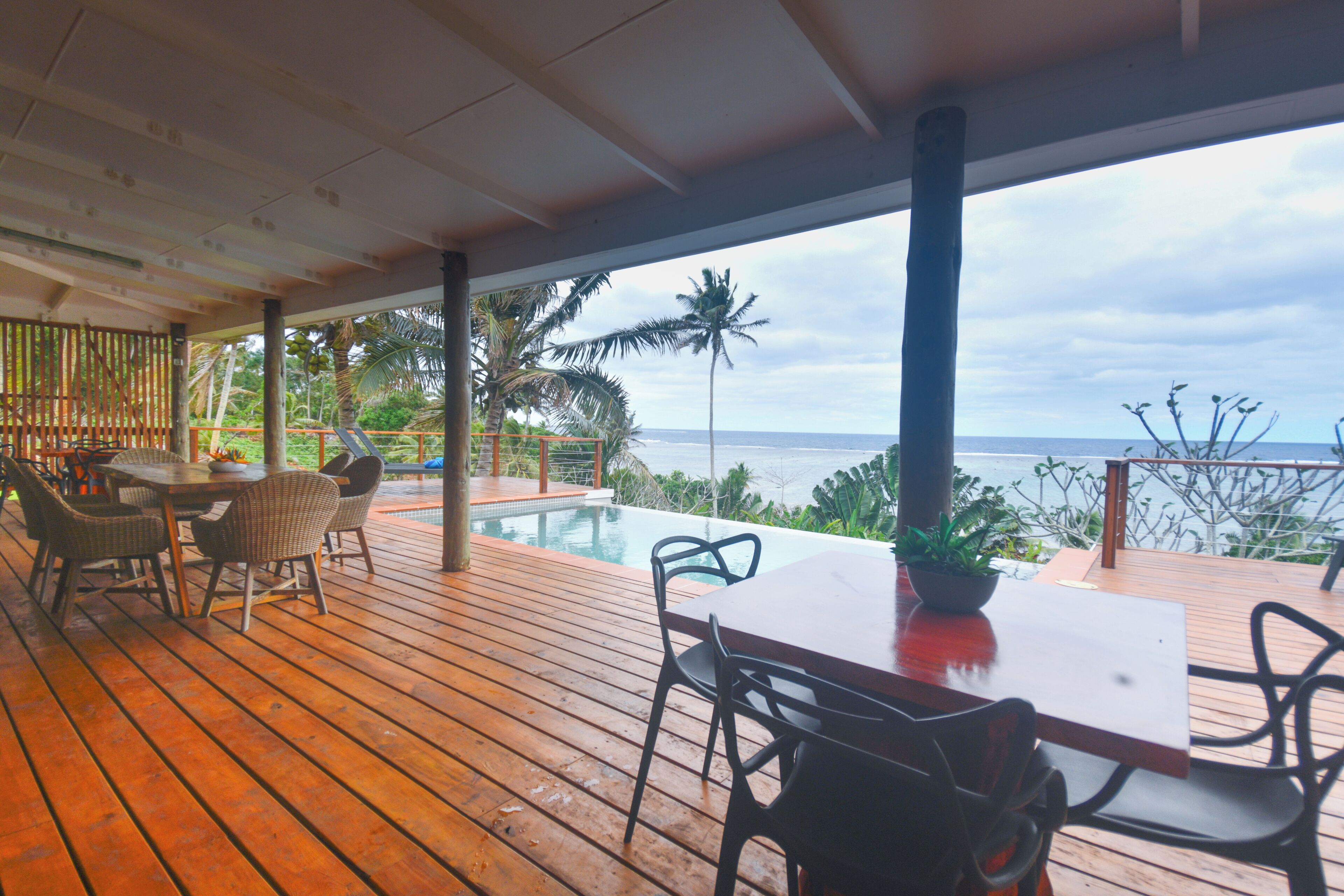 Eine Holzterrasse mit Pool, Stühlen und Tisch mit Blick auf einen Strand.