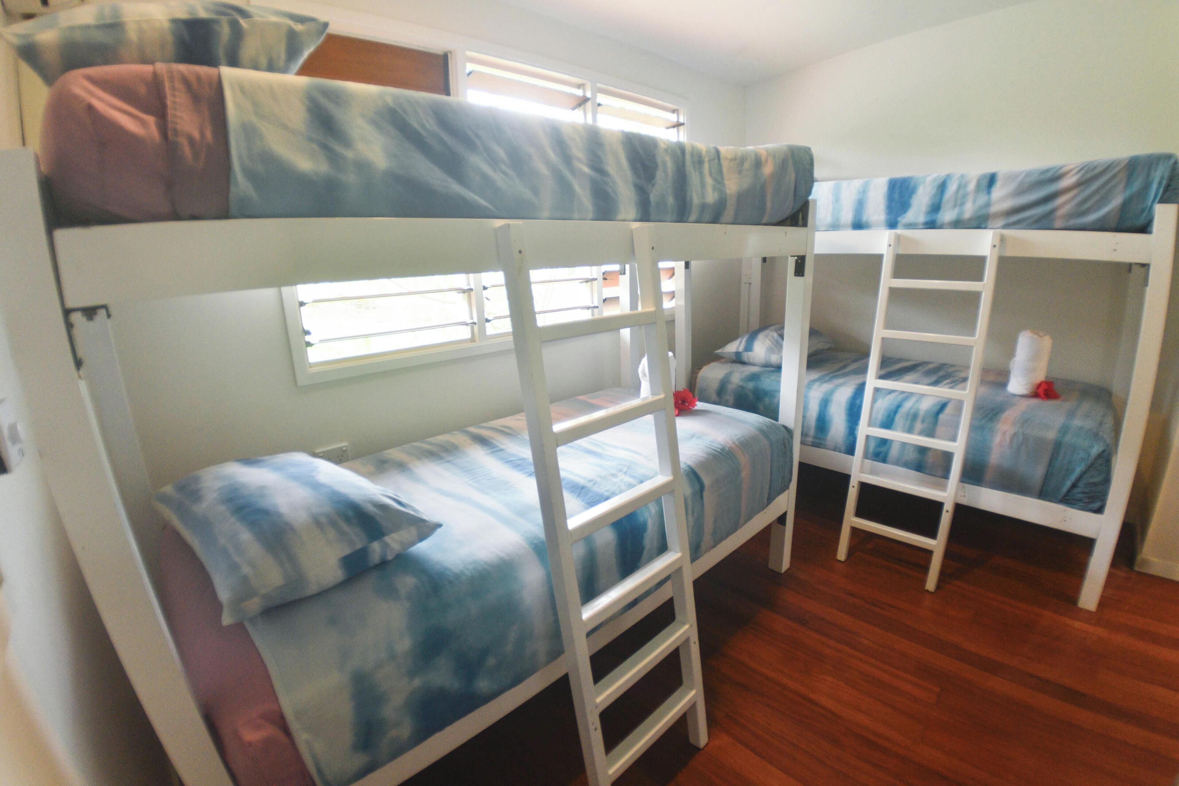 A bunk bed room with a window, wooden flooring, and a white wall.