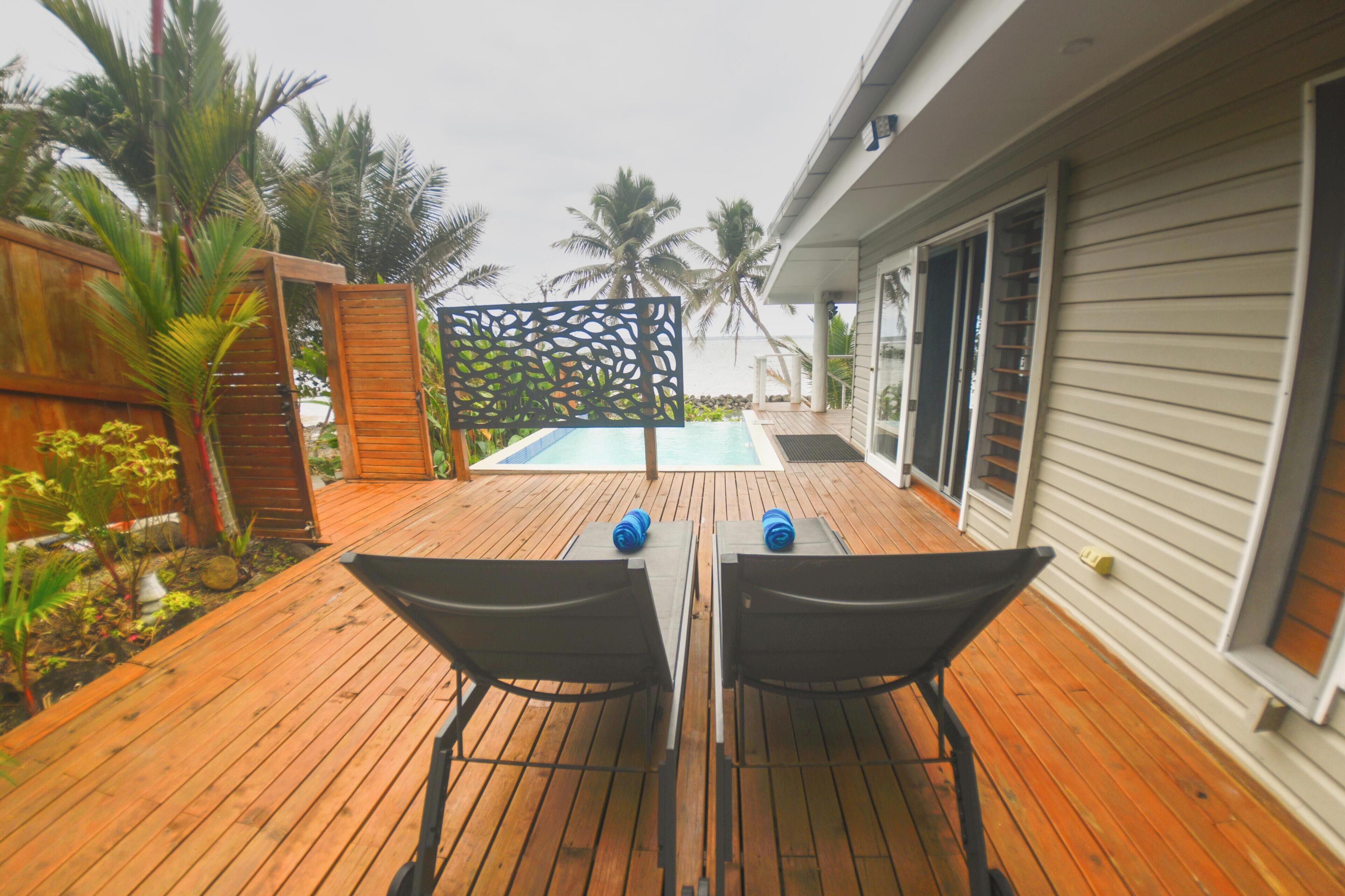 A wooden deck with a pool, two chairs, and a decorative screen.