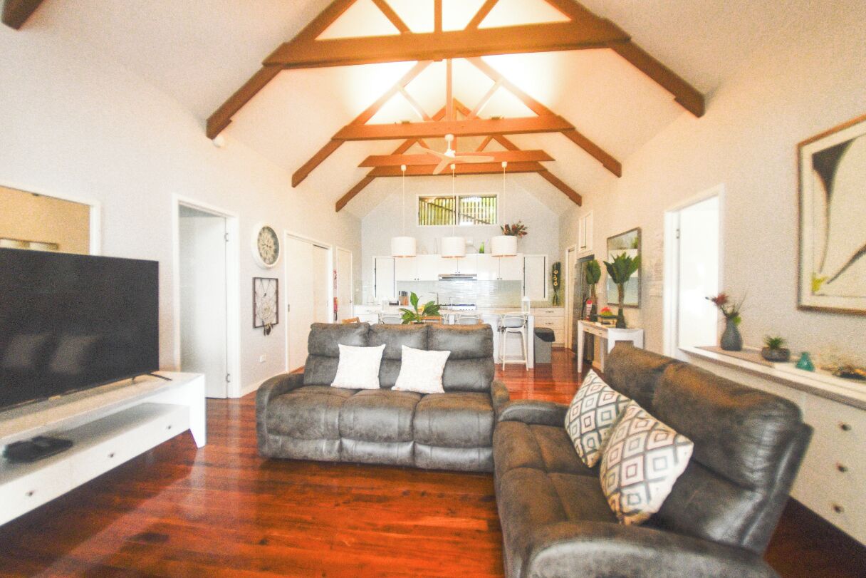 A living room with a television, two sofas, wooden flooring, and a kitchen in the background.