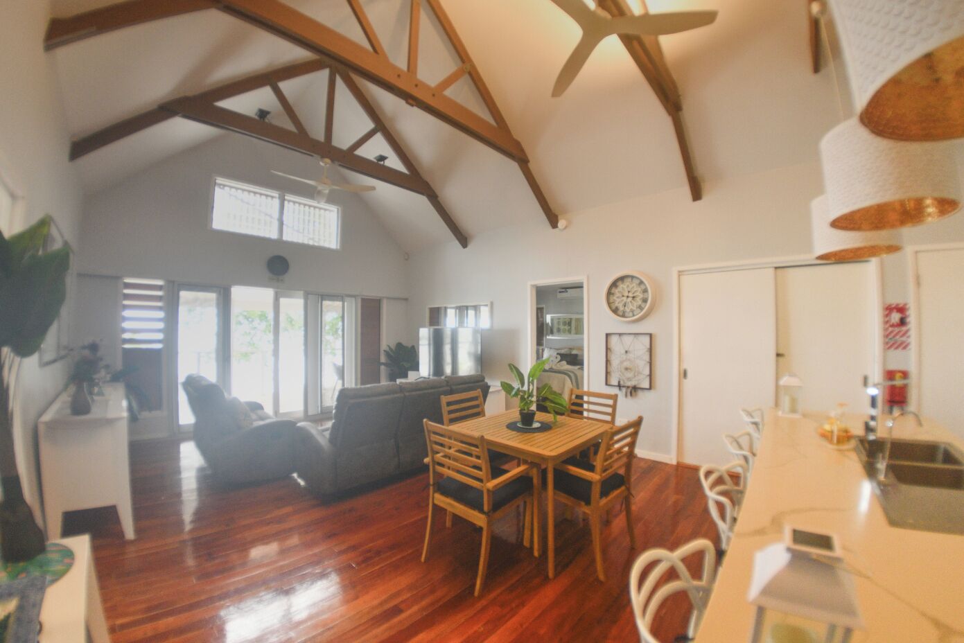 A spacious living area with a wooden ceiling, a dining table with chairs, and a kitchen area with a sink and countertop.