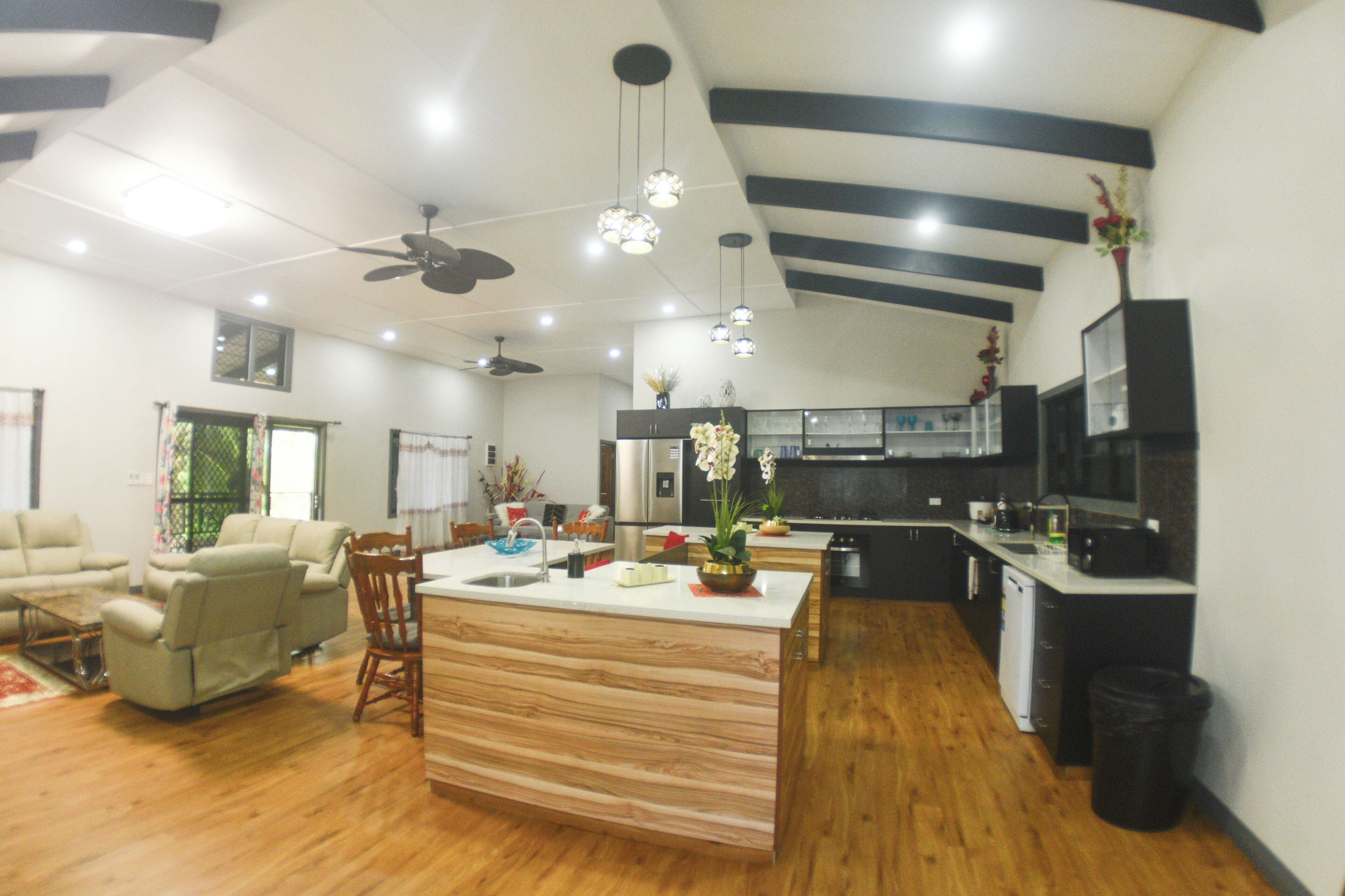 A modern kitchen with a central island, wooden flooring, and a ceiling fan.