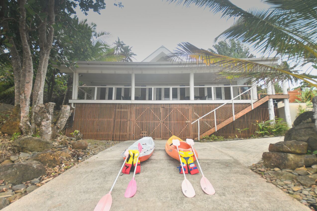 A building with a covered porch and a staircase leading to a wooden deck. Two kayaks with paddles are placed on the ground in front of the building.
