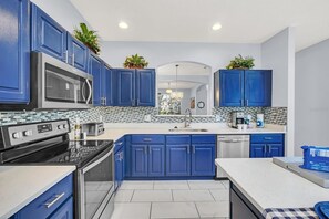 A modern kitchen with blue cabinets, stainless steel appliances, and a tiled backsplash. - Luxury 6 Bedroom Pool Home Near Disney (Kissimmee)
