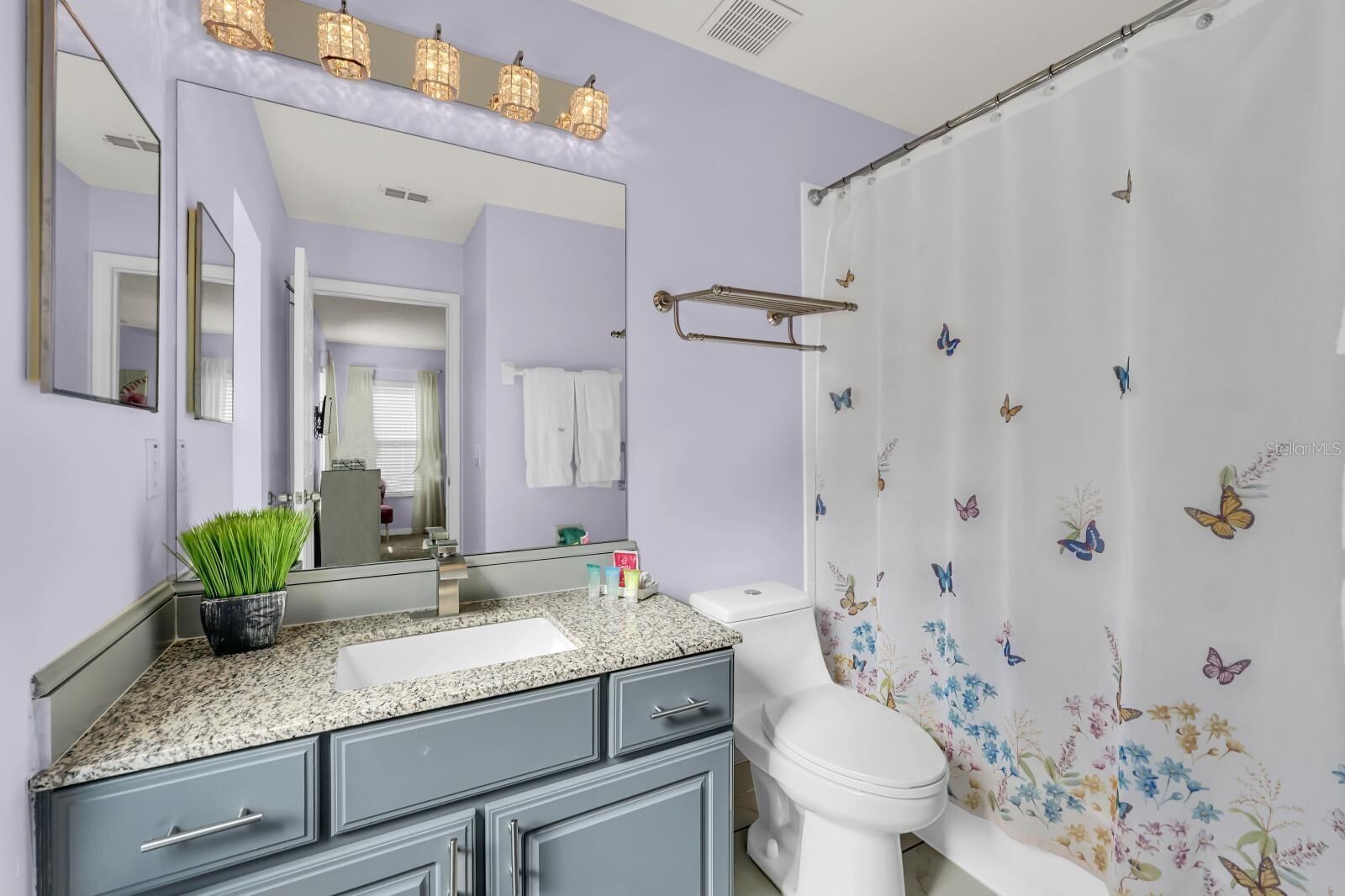 Un bagno con il water bianco, un lavabo con piano in granito, uno specchio illuminato e una tenda da doccia con motivo a farfalla.