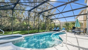 Ein Pool im Freien mit geschwungener Form, umgeben von einer überdachten Liegefläche mit Stühlen und Sonnenschirm.