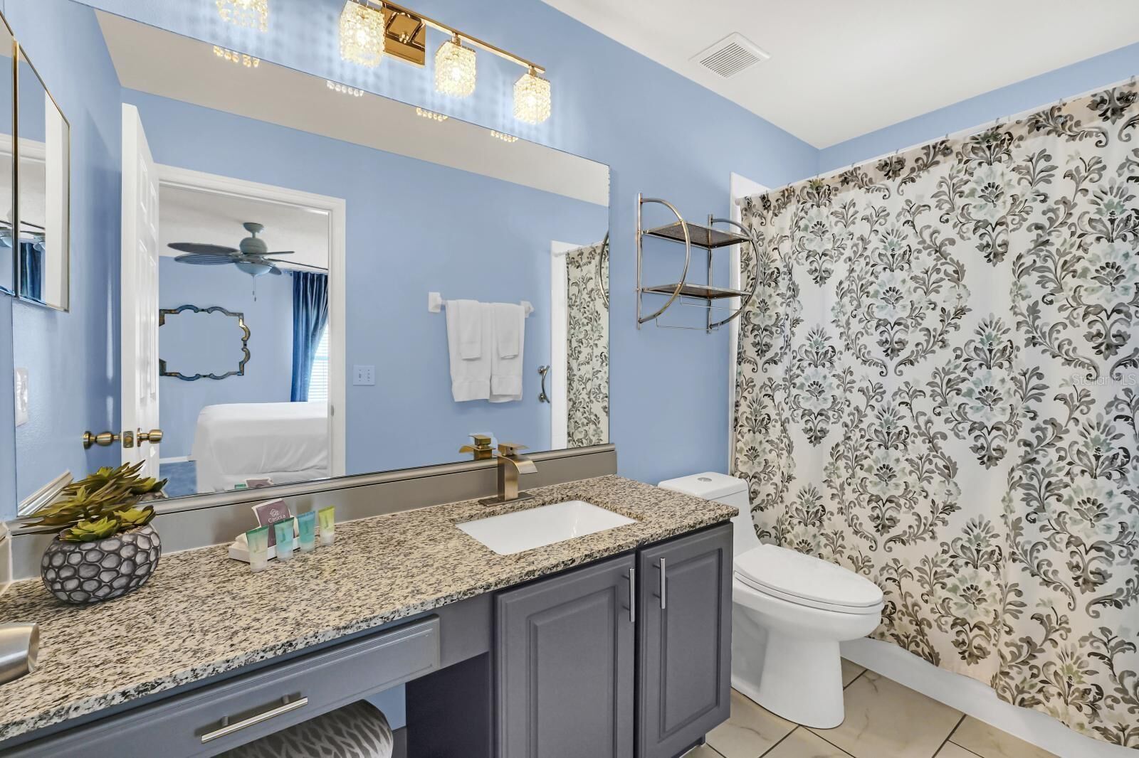 Un baño con encimera de granito, lavamanos blanco, inodoro y cortina de ducha estampada con motivos florales.