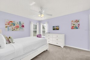 A bedroom with a bed, a dresser, a ceiling fan, and floral artwork on the walls. - Luxury 6 Bedroom Pool Home Near Disney (Kissimmee)