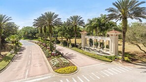 A paved road leading to a resort entrance with palm trees and a decorative archway. - Luxury 6 Bedroom Pool Home Near Disney (Kissimmee)