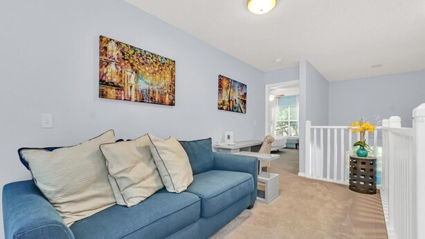 Ein Wohnzimmer mit einem blauen Sofa, zwei Bildern an der Wand, einer weißen Geländer und einem kleinen Tisch mit einer Blumenvase.