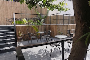 Un espace extérieur aménagé en terrasse, avec une clôture en bambou, des chaises et des tables en métal.