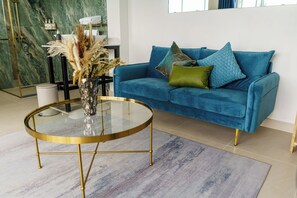 Un salon moderne avec un canapé bleu, une table basse en verre et un vase contenant des plantes séchées.