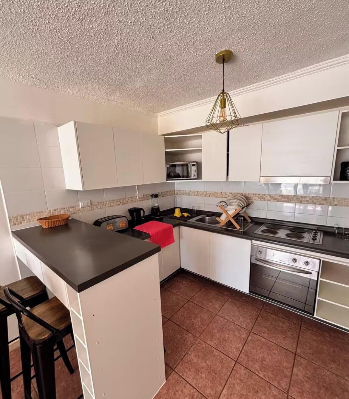 A compact kitchen with white cabinets, a black countertop, a red towel, a microwave, a stove, and a sink.