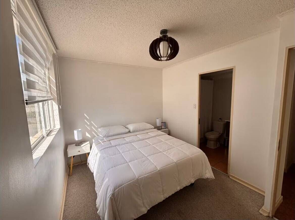 Ein Schlafzimmer mit einem Bett, einem Nachttisch, einer Lampe, einem Deckenventilator und einem Fenster mit Jalousien.