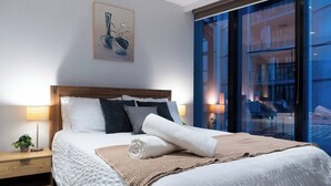 A modern hotel room with a large bed, a nightstand, a lamp, and a painting on the wall. - Luxury CBD LaTrobe Retreat 1BR Apt w/Pool & Gym (Docklands)