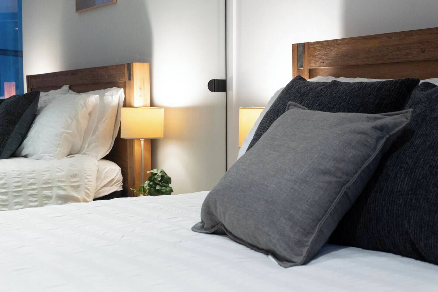 A hotel room with two beds, each with a wooden headboard, a bedside lamp, and a small plant.