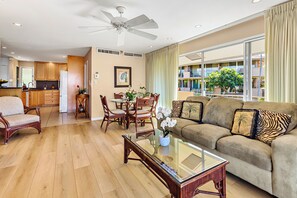 Ein modernes Wohnzimmer mit einem Glastisch, einer Couch mit gemusterten Kissen, Holzespeisestühlen und einem Deckenventilator.